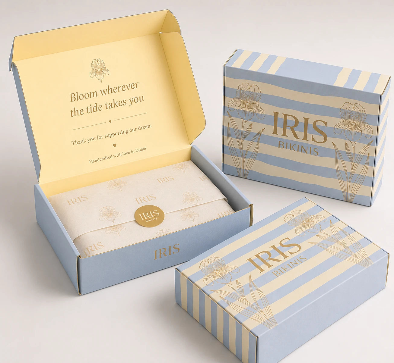 The IRIS box: powder-blue and butter stripes with gold iris line-art, tissue sealed with a gold IRIS sticker